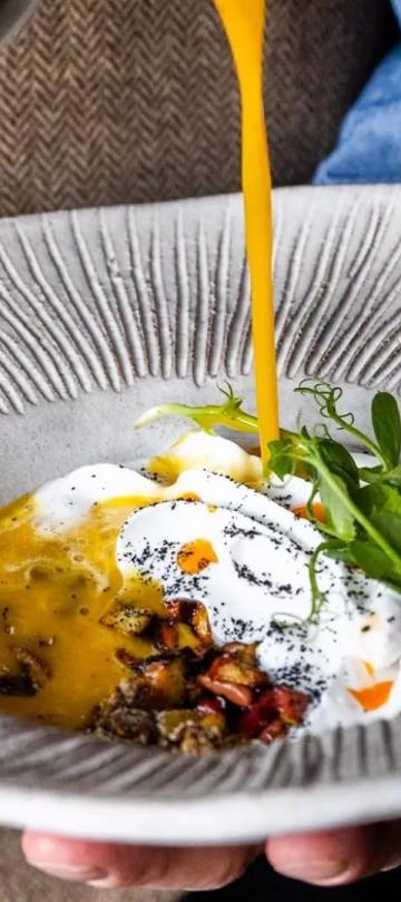 A server pour vinaigrette on an egg and greens dish
