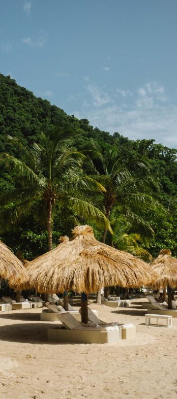 Beach recliners on Sugar Beach at the base of a mountain, each with thatched roof canopies