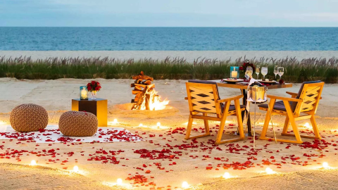 A table with wine and food setup on the beach with a fire and rose pedals laid on the ground at Viceroy Los Cabos