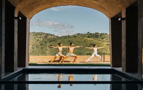 Three people doing yoga in a spa courtyard at Viceroy Ombria Algarve, with rolling hills in the background