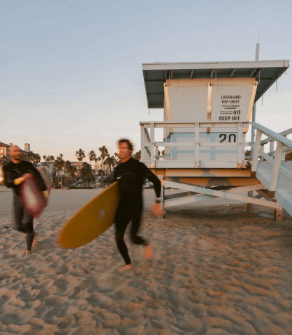 2 men running with surfboards on the beach at Viceroy Santa Monica