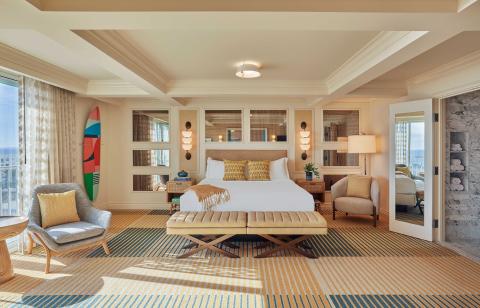 A beautiful large room at Viceroy Santa Monaca with a large bed, two lounge chairs, and a surf board on the wall