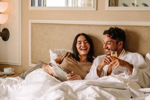 A couple laying in bed with the paper and a mimosa