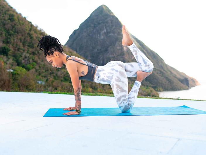 A woman doing a yoga pose on a mat, with the Pitons in the background