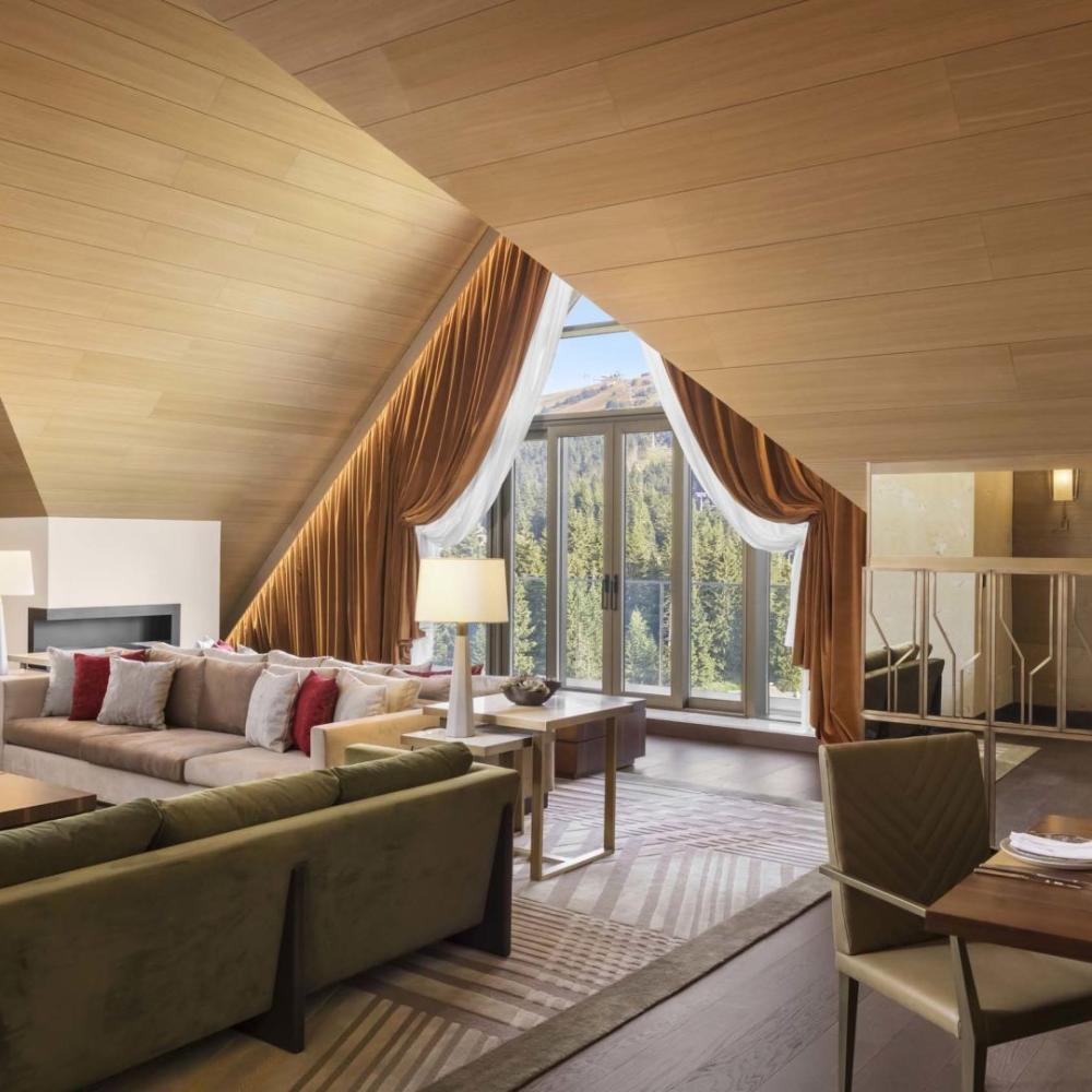 The living space of a penthouse suite with 2 couches, a large dining table and unique drop ceilings