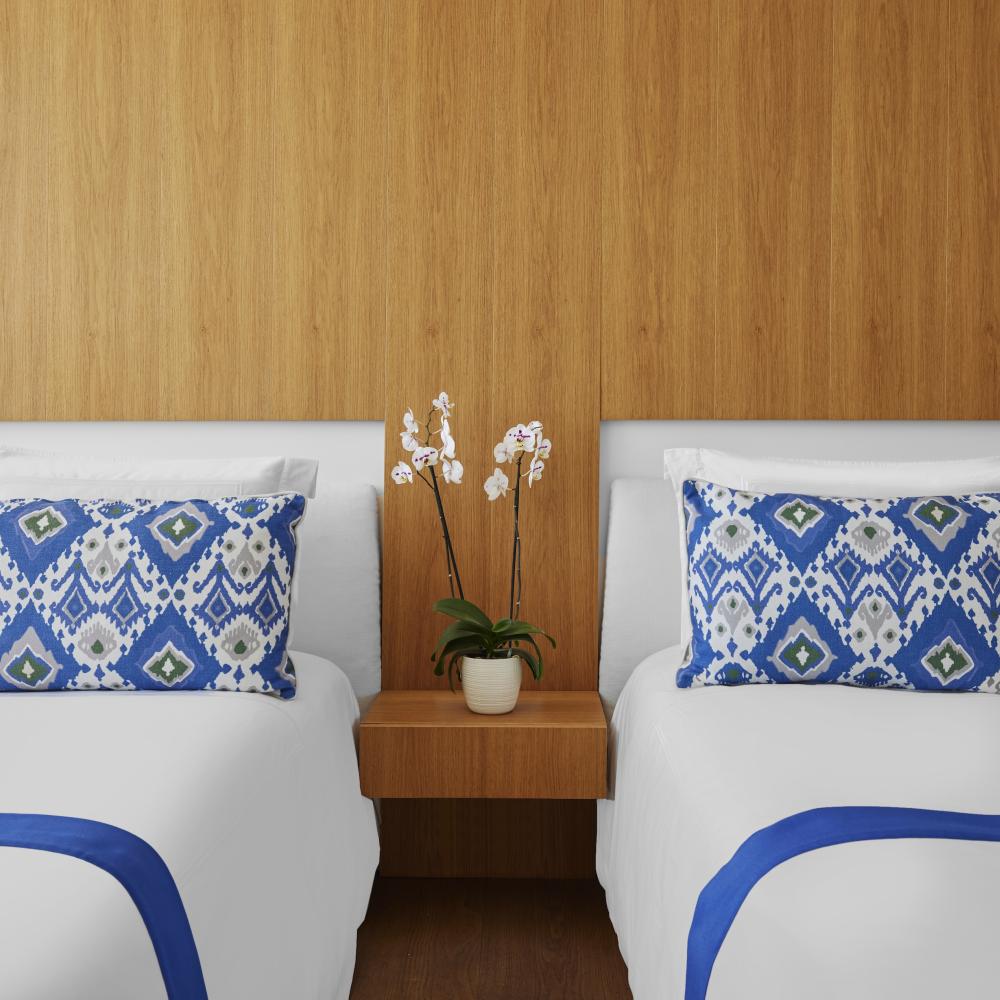 two beds with white and blue bedding separated by bedside table with potted flower