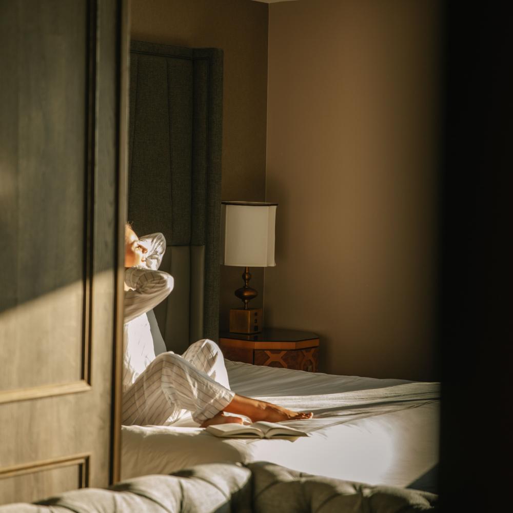 A woman relaxing in a Viceroy Washington DC guestroom, as sun streams through the window