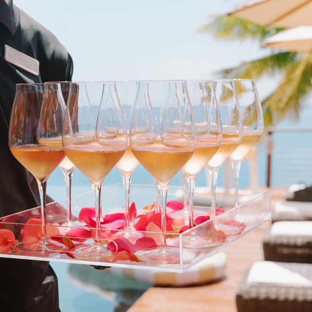 Des verres à vin disposés sur un plateau parsemé de pétales de fleurs