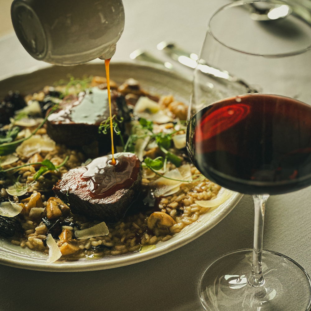 Une assiette de mets raffinés accompagnée d'un verre de vin rouge, élégamment disposée sur une table à manger.
