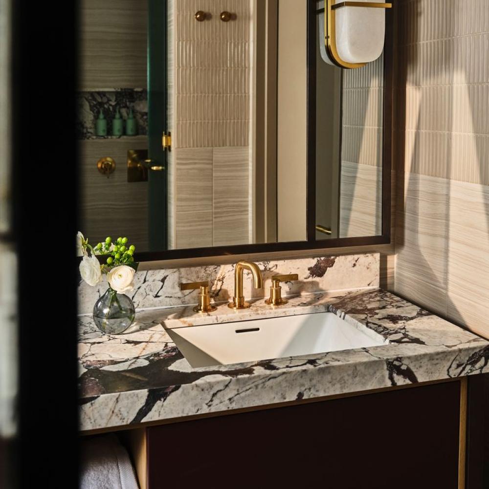 Bathroom vanity with a white rectangular sink, gold faucet, veined marble countertop, large mirror, and wall sconce.