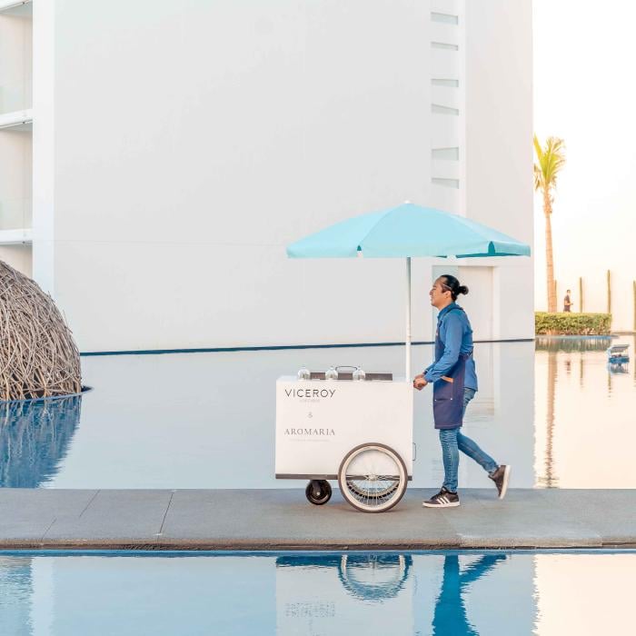 staff member pushes a small white cart with blue umbrella between two pools