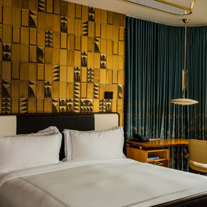 A hip hotel room at Viceroy Chicago, with a large bed and an accent wall made of textured gold panels