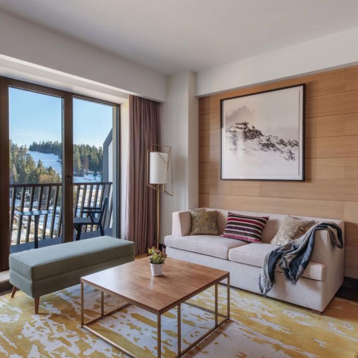 The living soace in a suite with a couch, desk, bench, and access to a balcony at Viceroy Kopaonik Serbia