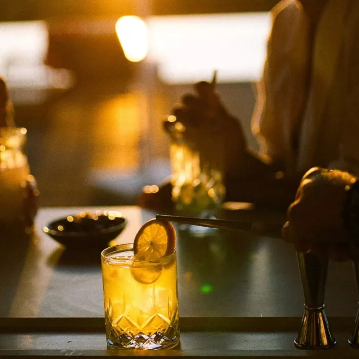 Patrons at Salpico Pool Bar enjoy a bright orange drink with an orange garnish, at dusk