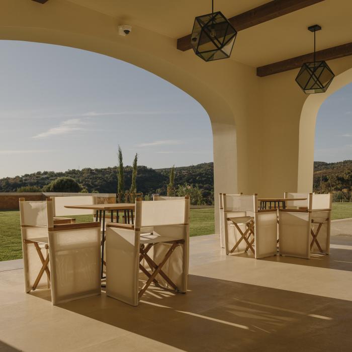 A sunny arched courtyard at Viceroy Ombria Algarve, featuring two tables surrounded by wood chairs, in view of the Algarve countryside