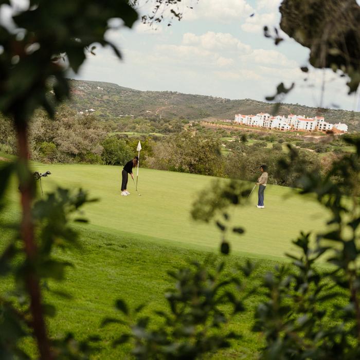 Dois jogadores no green do campo de golfe Ombria, com Viceroy Ombria Algarve fundo