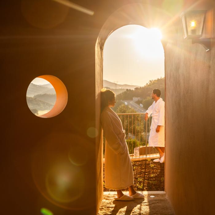 A couple in bathrobes looks out on the Algarve countryside through a rounded arch doorway