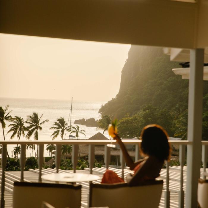 A woman enjoys a drink on a shaded patio overlooking the beach