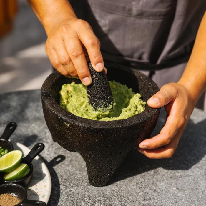 A man makes guacamole in a stone molcajete