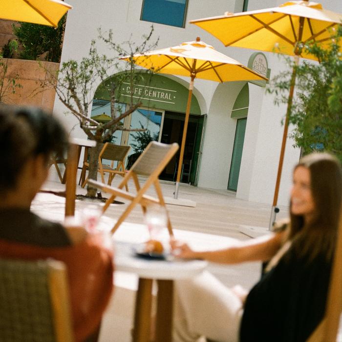 two people sit at tables in courtyard under yellow umbrella
