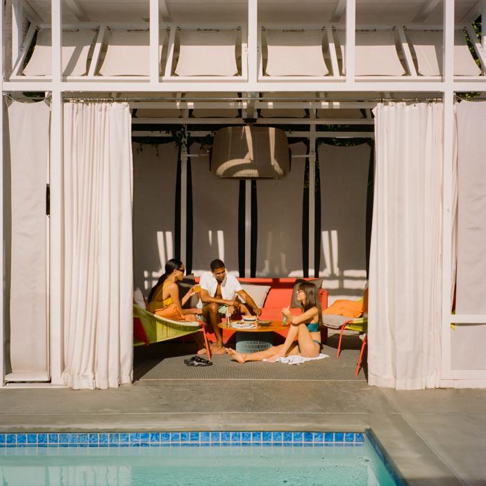 Three friends sit in a cabana, sipping drinks and talking.