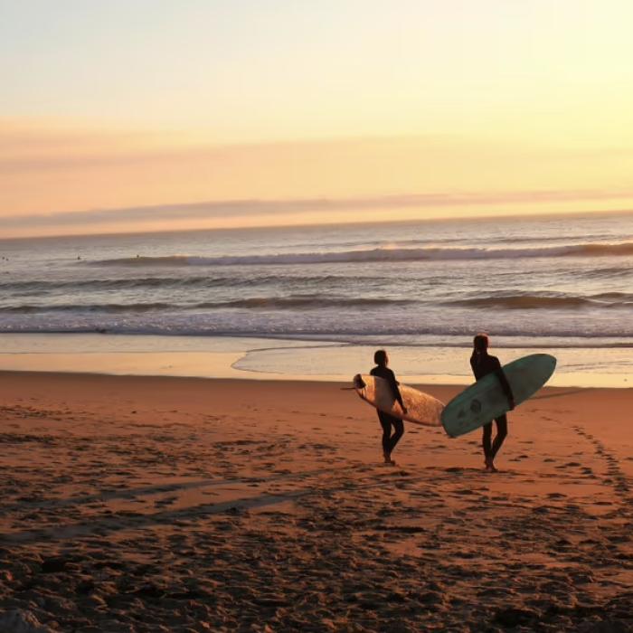 Two people walking at sunrise on a Los Cabos beach with surf boars