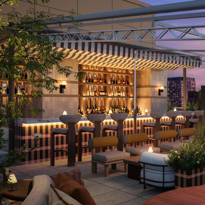 A rooftop restaurant patio at dusk has a bar, cushioned seating, round tables, planters, and a metal canopy overlooking city buildings.