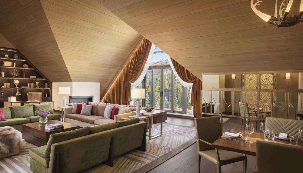 The living space of a penthouse suiter with 2 couches, a large dining table, a floor to ceiling bookshelf and unique drop ceilings A washroom with a large double sink vanity and a soaker tub in a penthouse suite at Viceroy Kopaonik Serbia