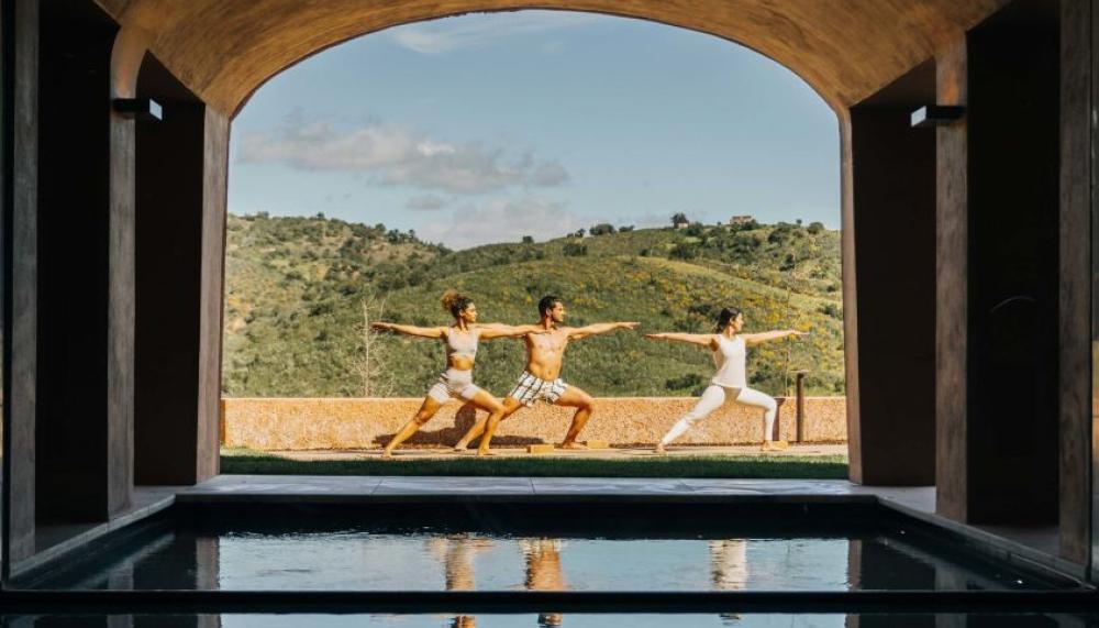 Three people doing yoga in a spa courtyard at Viceroy Ombria Algarve, with rolling hills in the background