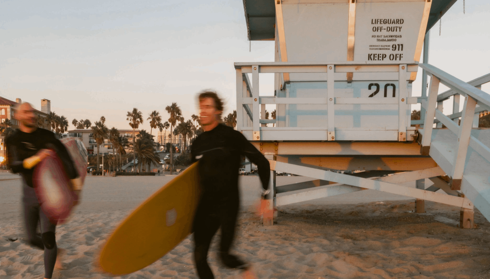 2 men running with surfboards on the beach at Viceroy Santa Monica