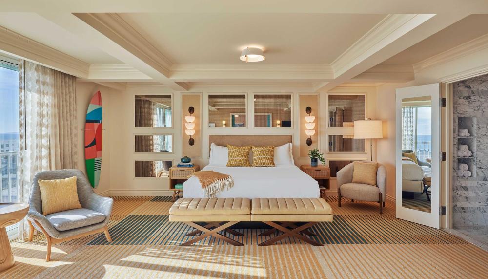 A beautiful large room at Viceroy Santa Monaca with a large bed, two lounge chairs, and a surf board on the wall 