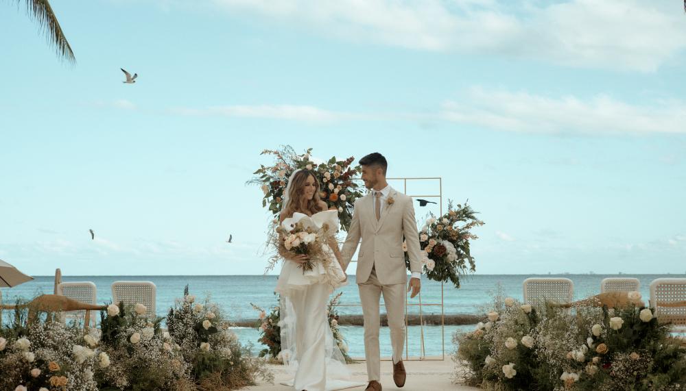 A newly married couple walk hand in hand back down the aisle, smiling at one another. 