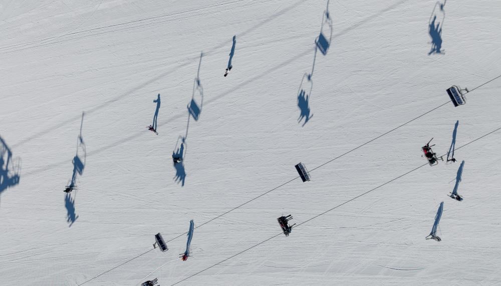 An aerial view of the ski lifts, with the shadows of the lift sharply contrasting the snow below