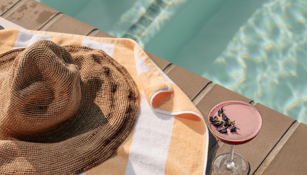 a poolside towel with books, a magazine, and cocktail