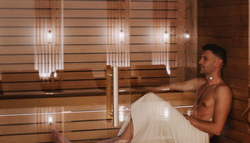 Um homem com uma toalha branca descansa num banco de madeira numa sauna moderna.