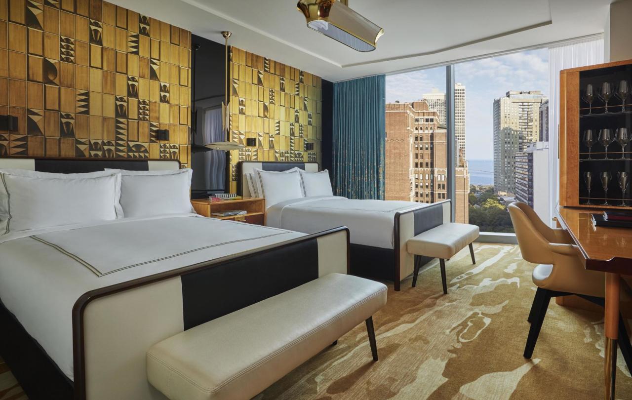 Two beds against an ornate gold accent wall in a Viceroy Chicago guestroom, with a large window looking out on the Gold Coast neighborhood