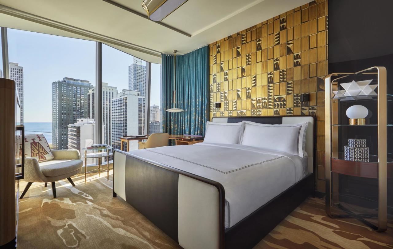 A King bedroom against an ornate gold accent wall in a Viceroy Chicago guestroom with a large window overlooking the Gold Coast neighborhood of Chicago