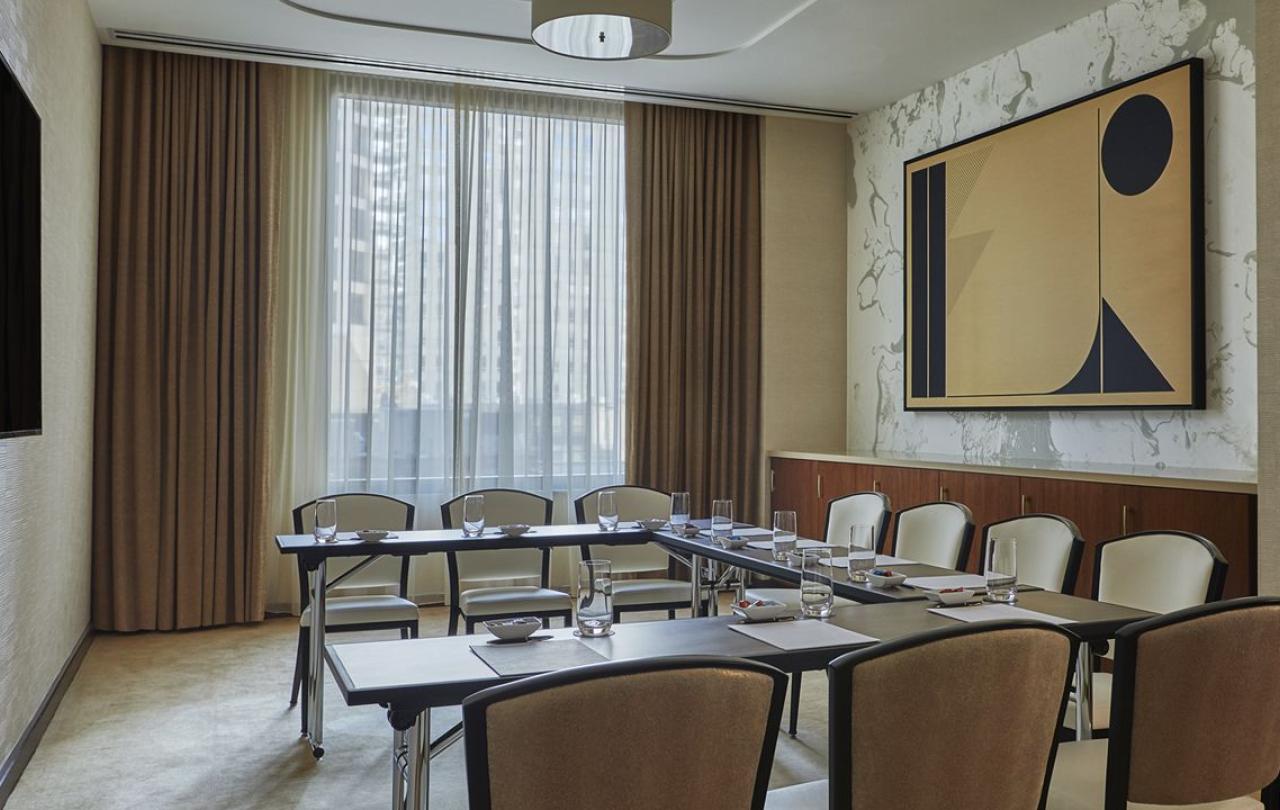 A meeting room at Viceroy Chicago, with rows of the desks and chairs organized in a U shape around a wall mounted television