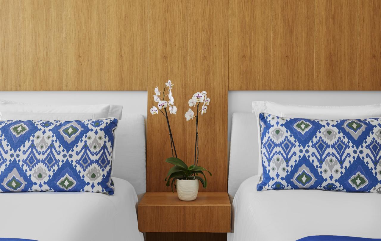 two beds with white and blue bedding separated by bedside table with potted flower