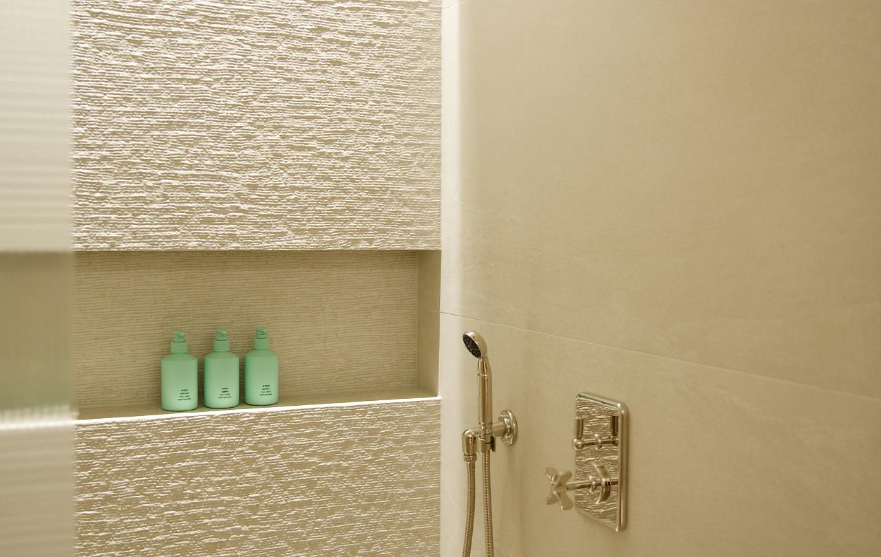 Luxurious walk-in hotel shower featuring textured beige tile, modern chrome fixtures, and bath products in a niche.