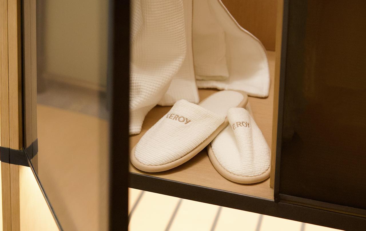 Close-up of white plush slippers embroidered with text inside an open wooden wardrobe shelf.