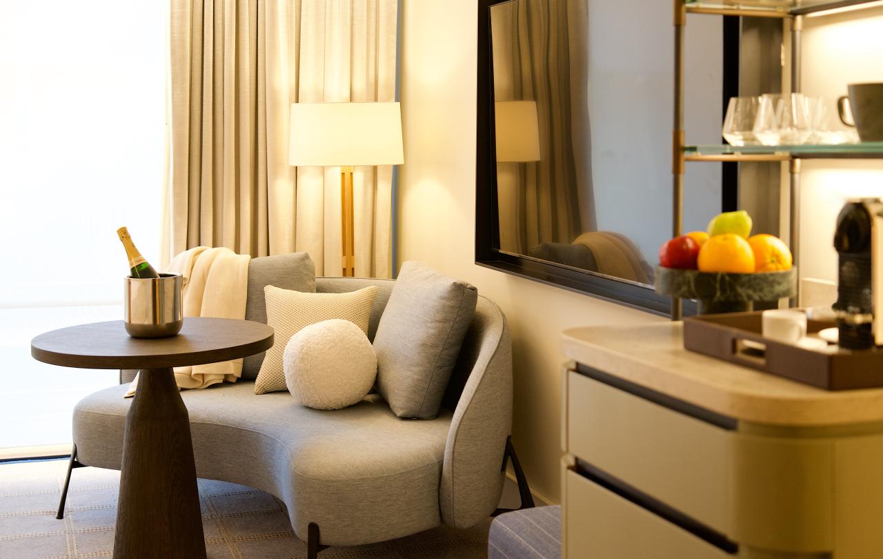 Curved grey sofa with throw pillows and table set with champagne beside a modern TV setup.