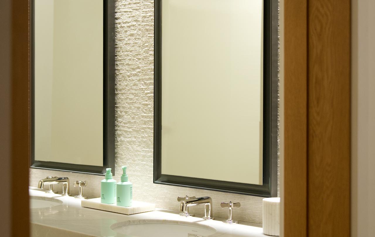 View through an open doorway of a hotel bathroom double vanity with two black-framed mirrors.