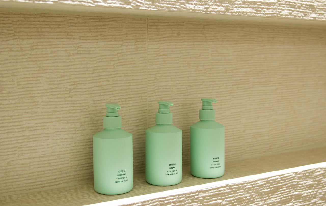 Three mint green amenity bottles sitting inside an illuminated tiled shower wall niche.