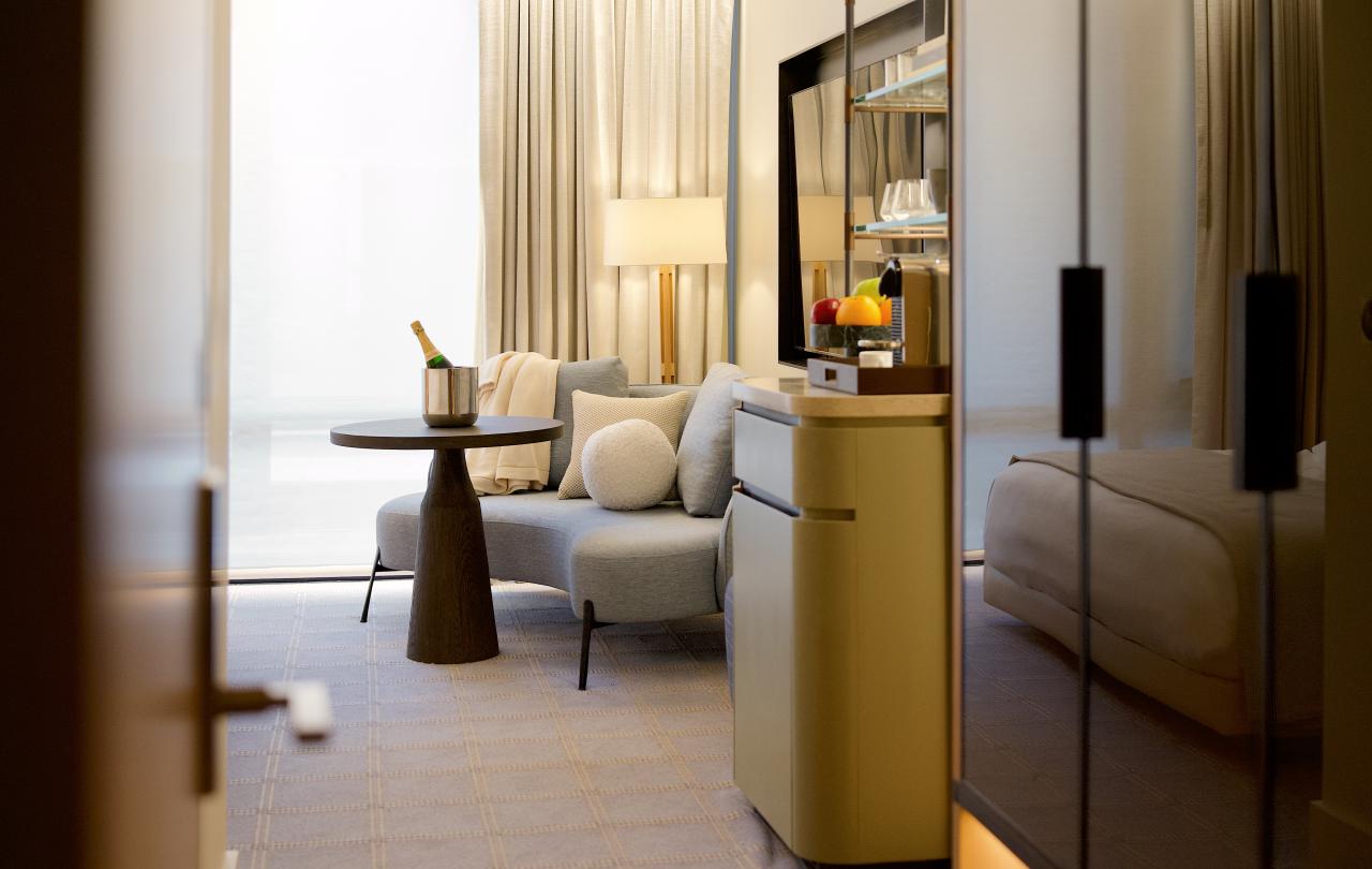 Elegant hotel room suite featuring a curved sofa, small dining table with champagne, and a king bed.