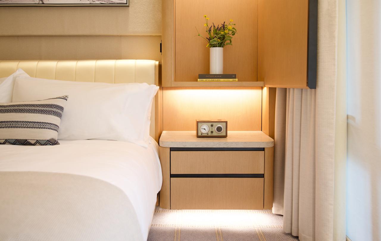 Close-up of a hotel bedside table with a vintage radio, warm under-cabinet lighting, and fresh flowers.
