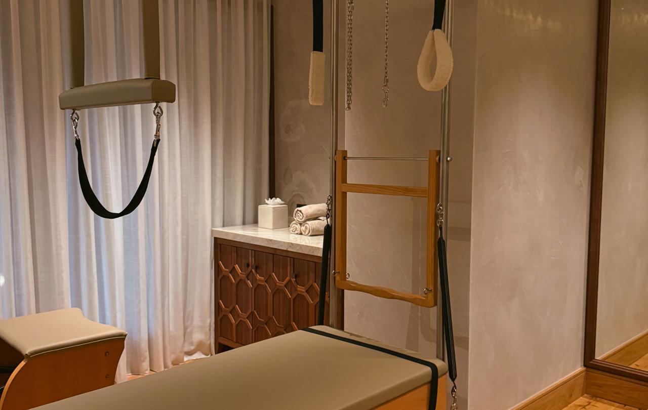 Cama de Pilates Reformer com um aparelho Cadillac e um trapézio suspenso num estúdio.