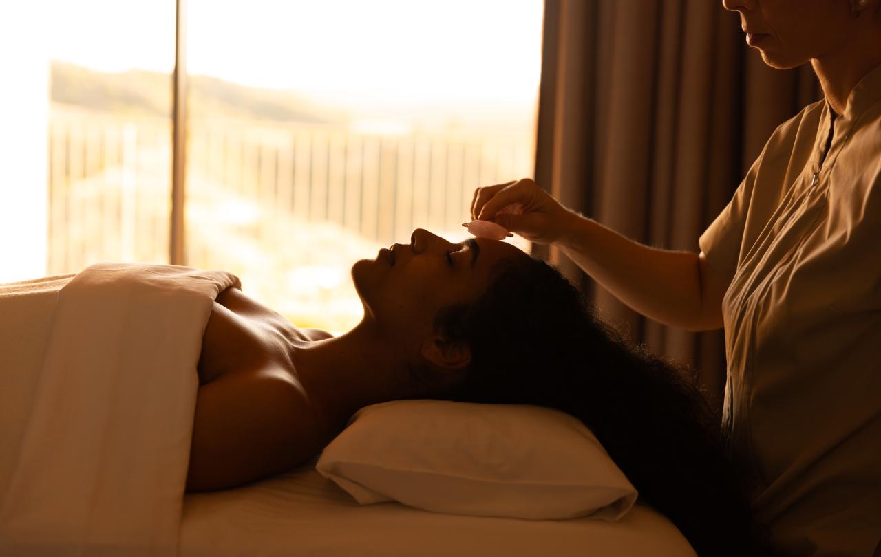 Perfil em silhueta de um cliente a receber um tratamento facial junto a uma janela iluminada pelo sol.