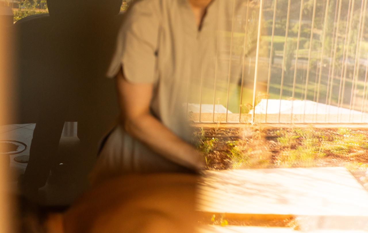 Reflexo banhado por uma luz acolhedora de um terapeuta a fazer uma massagem corporal junto a uma varanda com vista para a montanha.