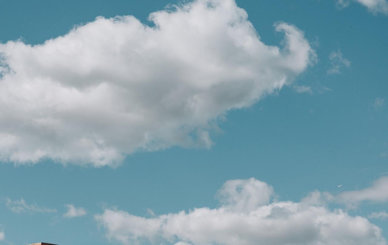 Telhado de telhas de barro e chaminé de um edifício, com um céu azul brilhante e nuvens brancas como pano de fundo.